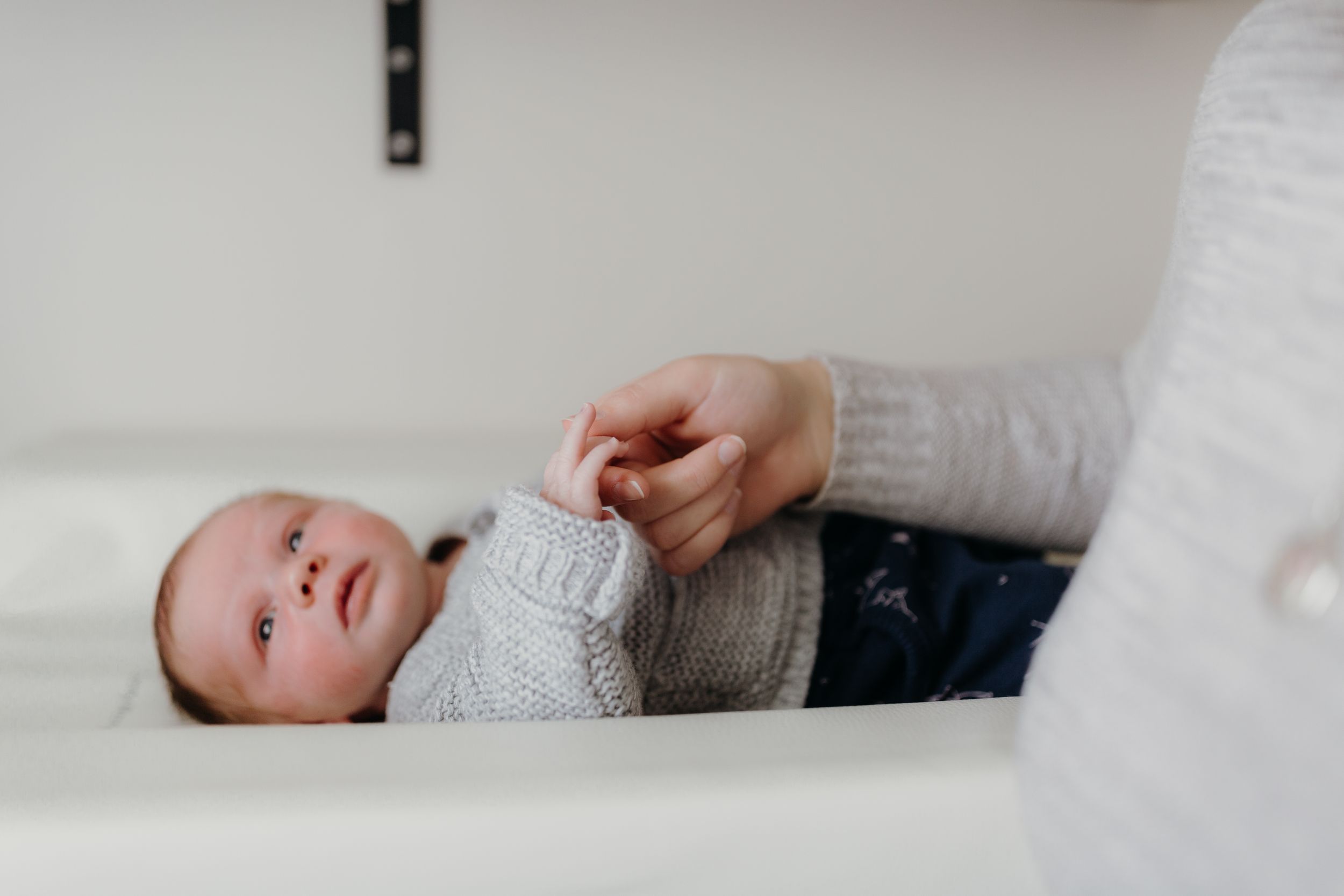 newborn lying on chase table holding mums hand