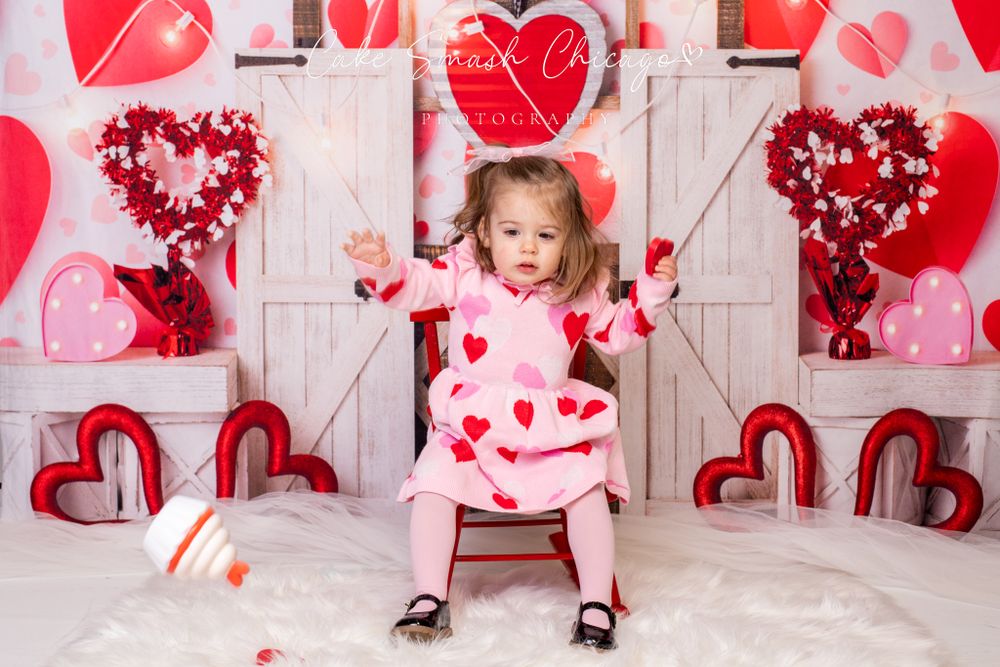 A smiling child dressed in Valentine's Day-themed outfits posing for the camera during a Valentine's miniv