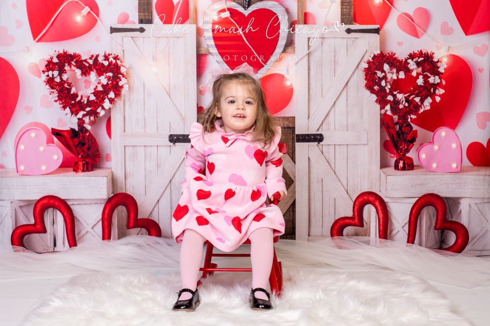 A smiling child dressed in Valentine's Day-themed outfits posing for the camera during a Valentine's mini