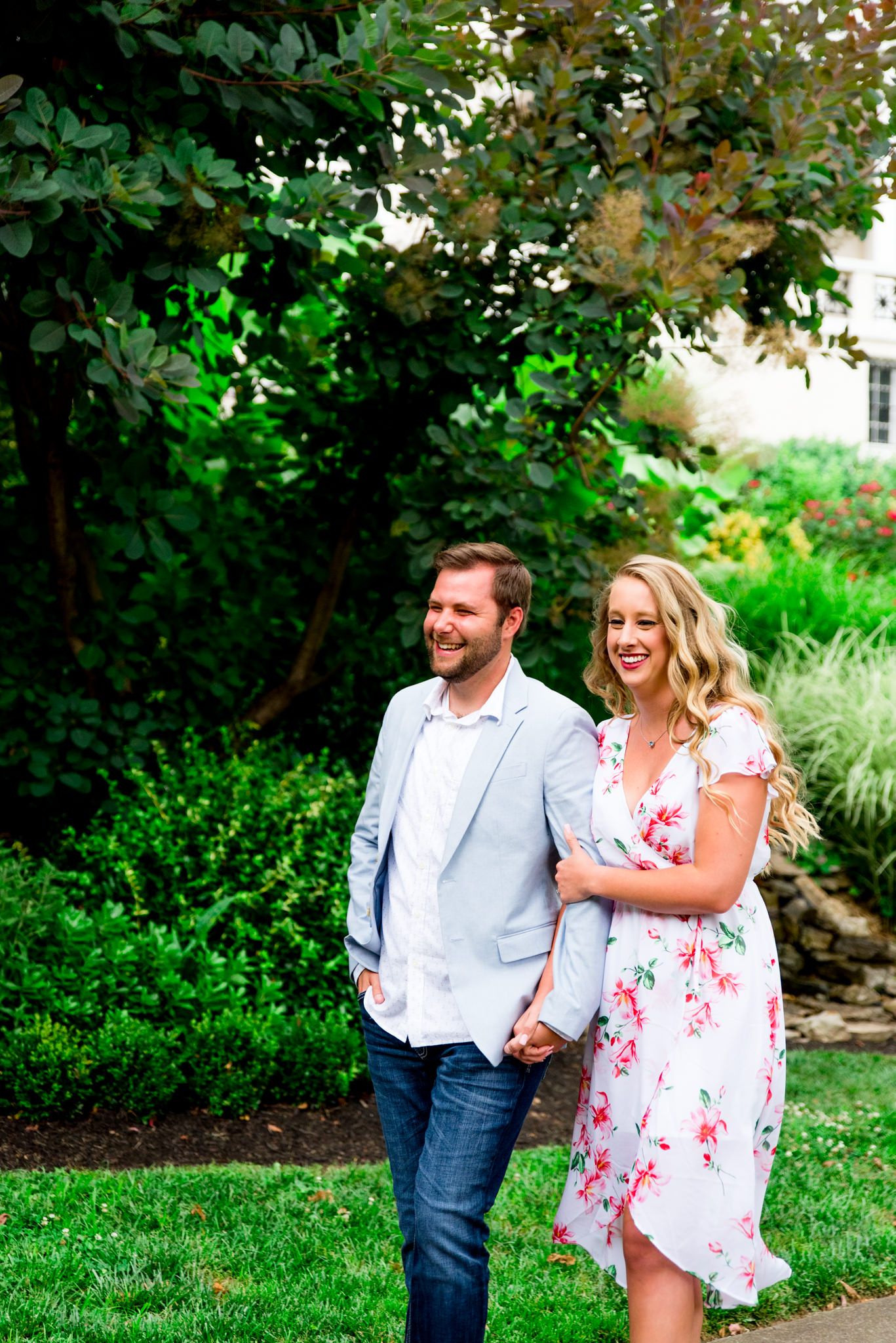 engaged couples in floral dress and light blue suit jacket and jeans walking in rainy Louisville and laughing
