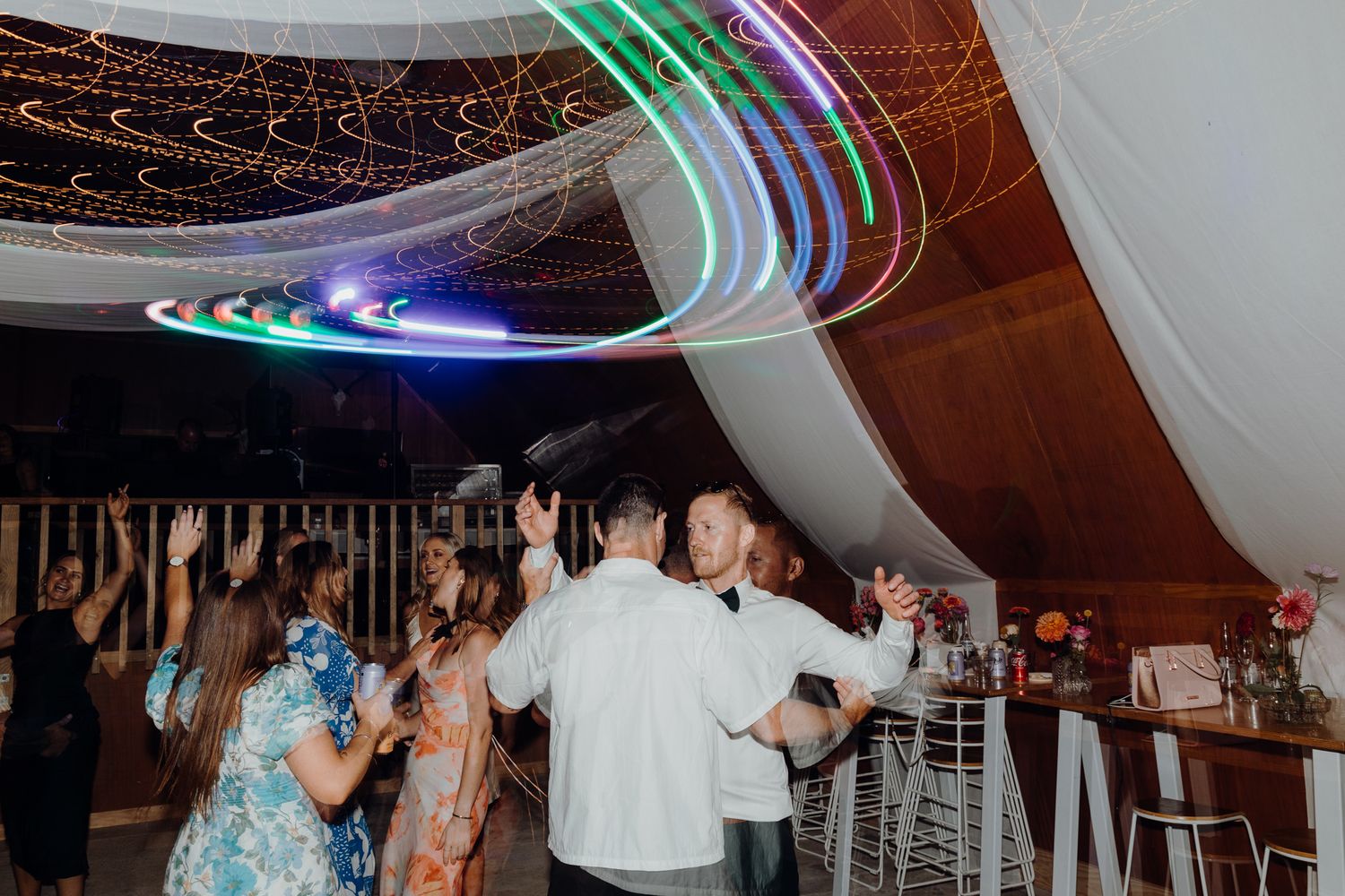 Lively wedding dance floor with colorful light trails and white ceiling decorations.