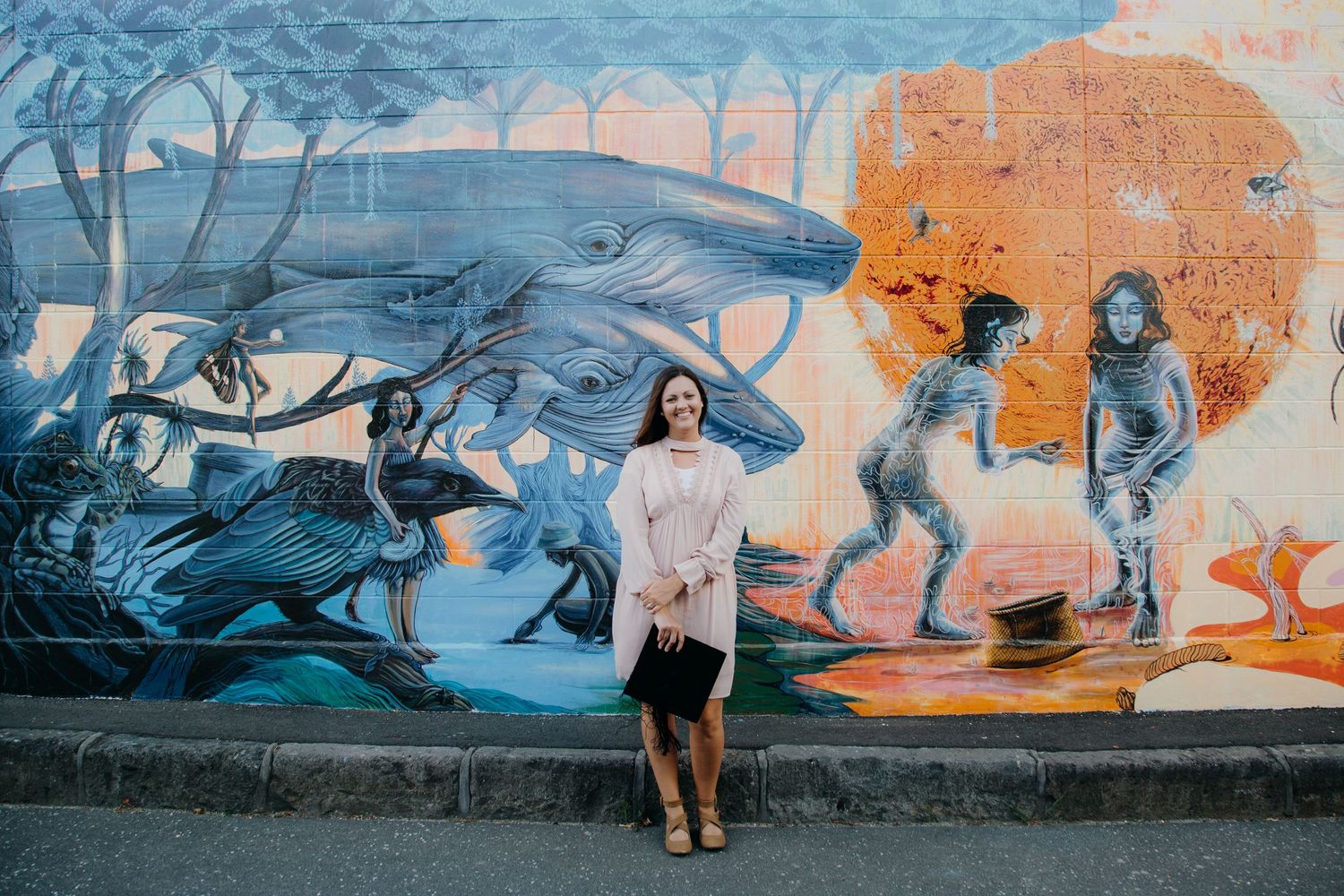 graduate standing infront of maori art mural holding graduation cap