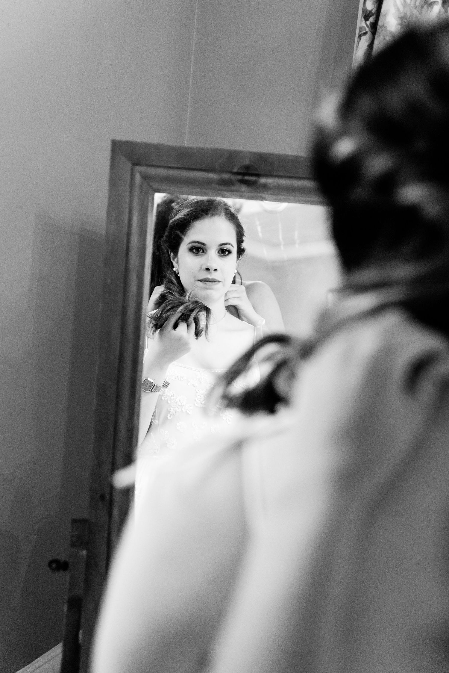 bride looks in the mirror at herself while bridesmaid puts necklace on her