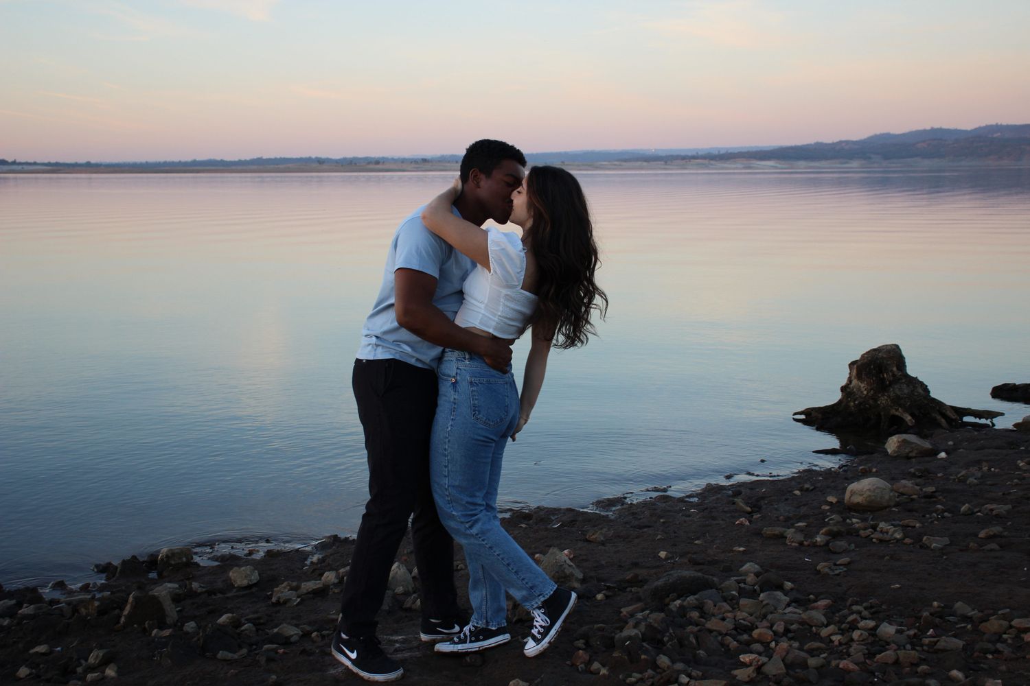 Couple engaged kissing in front of a lake at sunset