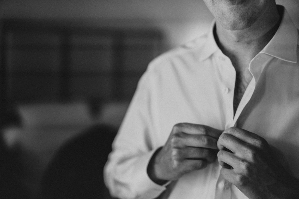 Groom buttons up his shirt as he gets ready for the wedding ceremony