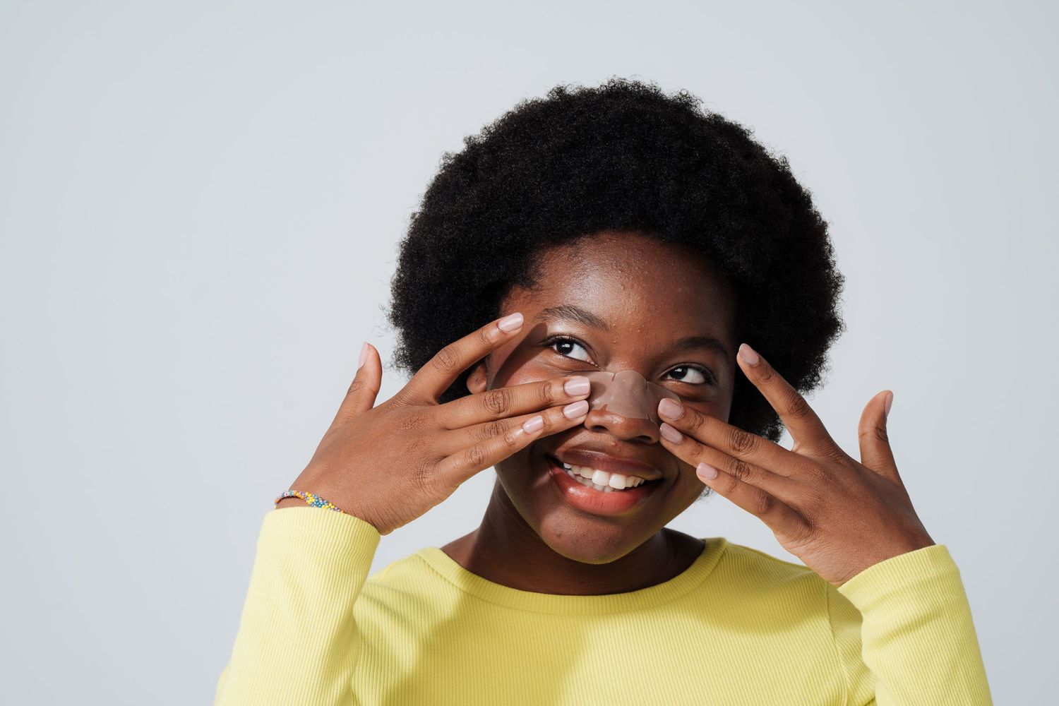 Person in yellow sweater playfully covering parts of their face while smiling.