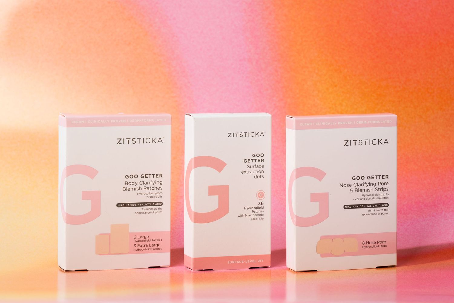 Three Zitsticka product boxes arranged on pink and orange gradient surface.