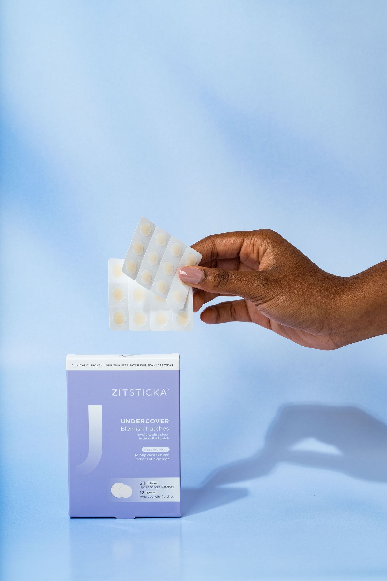 Hand holding skincare patches against blue background with Zitsticka product box.
