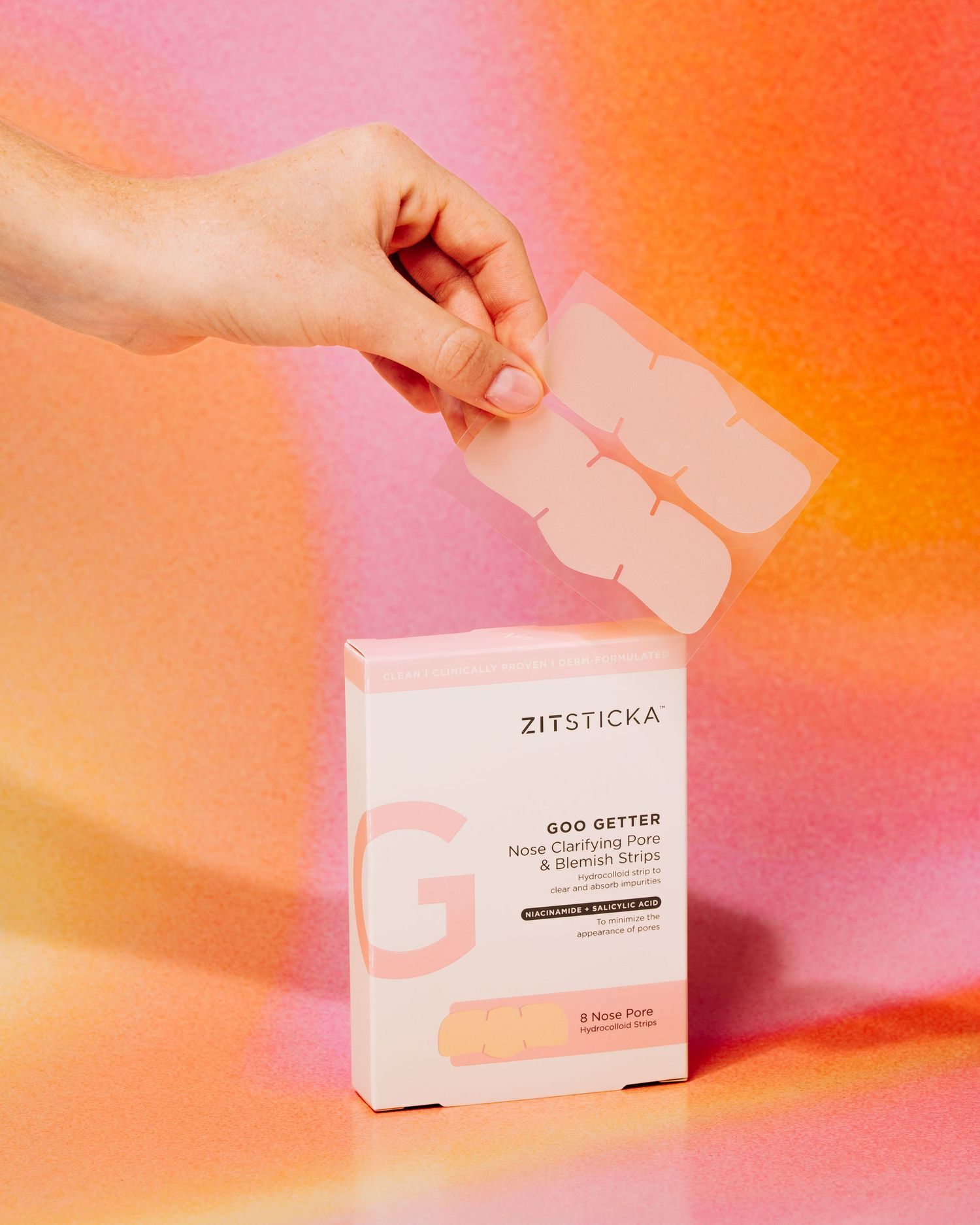 Zitsticka acne patches being held against a pink and orange gradient background.