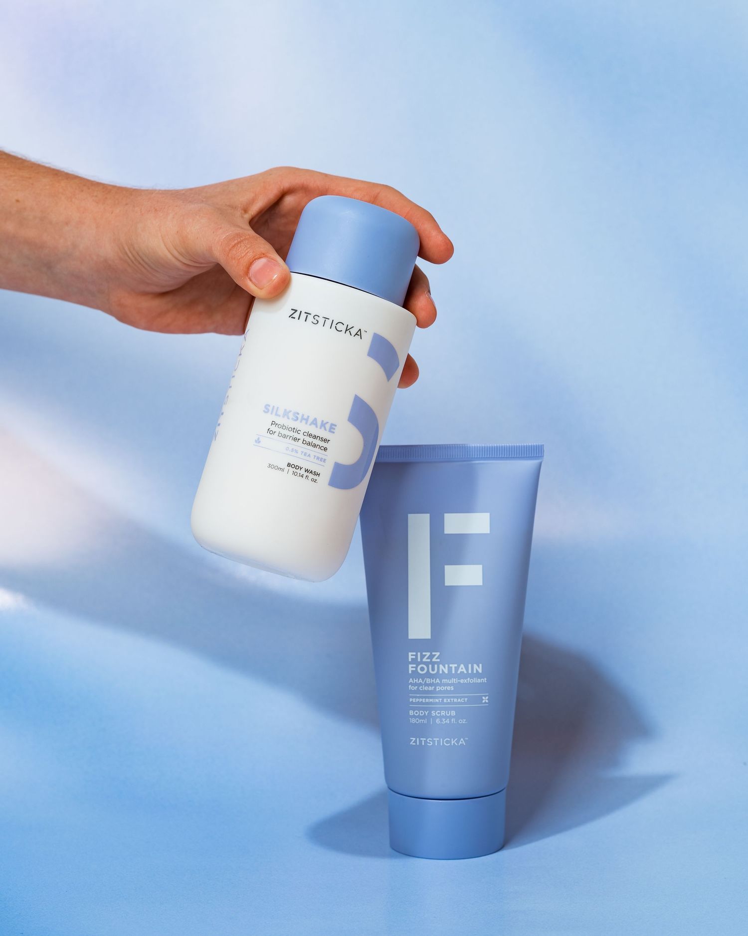Hand reaching for blue and white skincare products against light blue background.