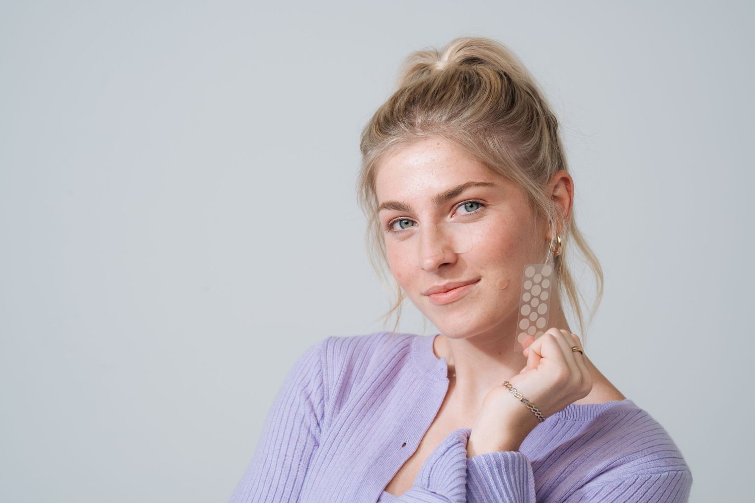 Person wearing lavender sweater posing against grey background.