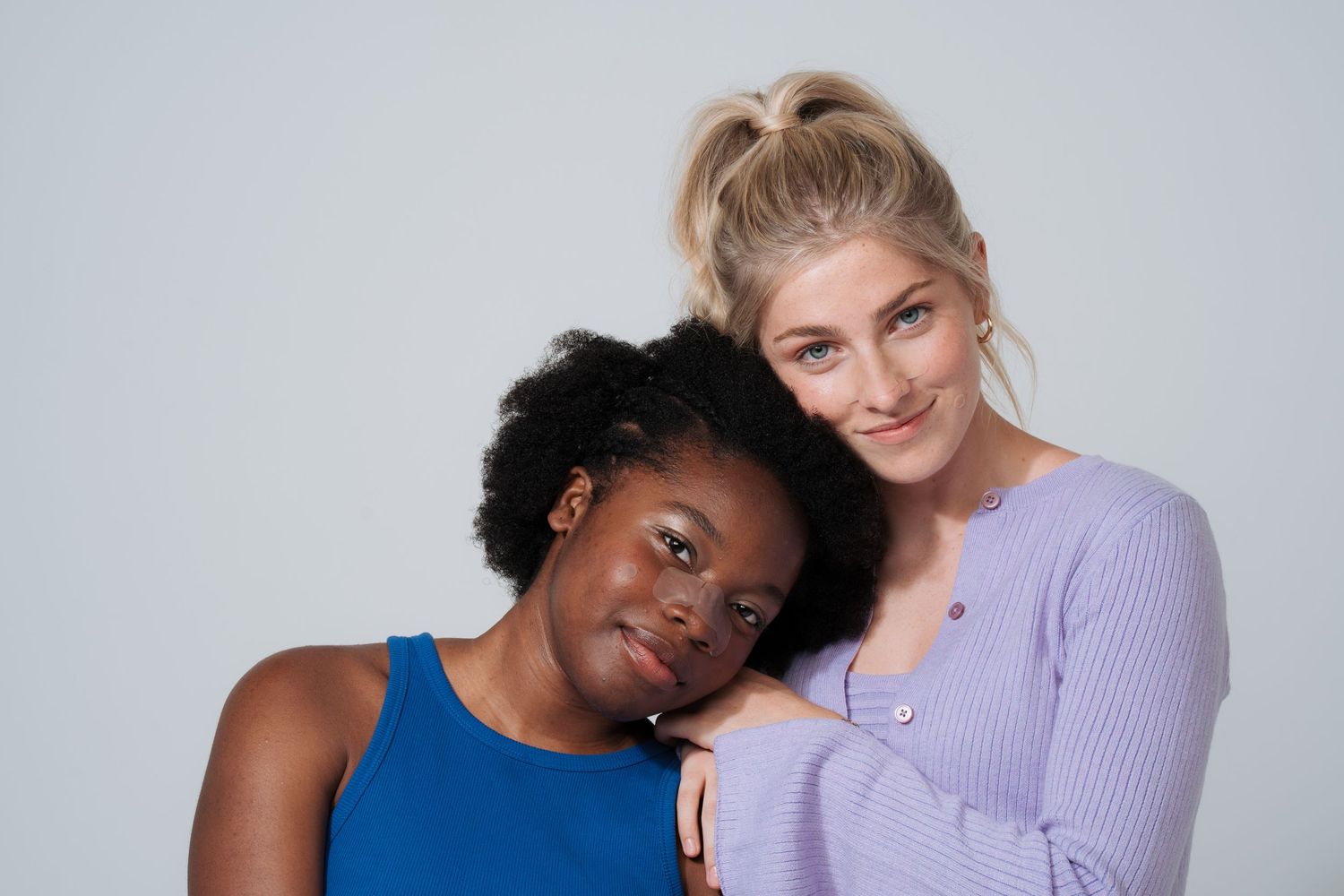 Two people in casual attire smiling together against grey background.