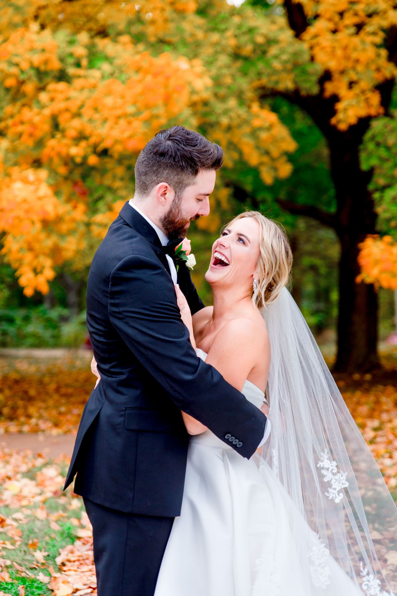 bride with lace veil leaning on grooms chest, who is hugging her in front of orange tree for STL wedding pictures
