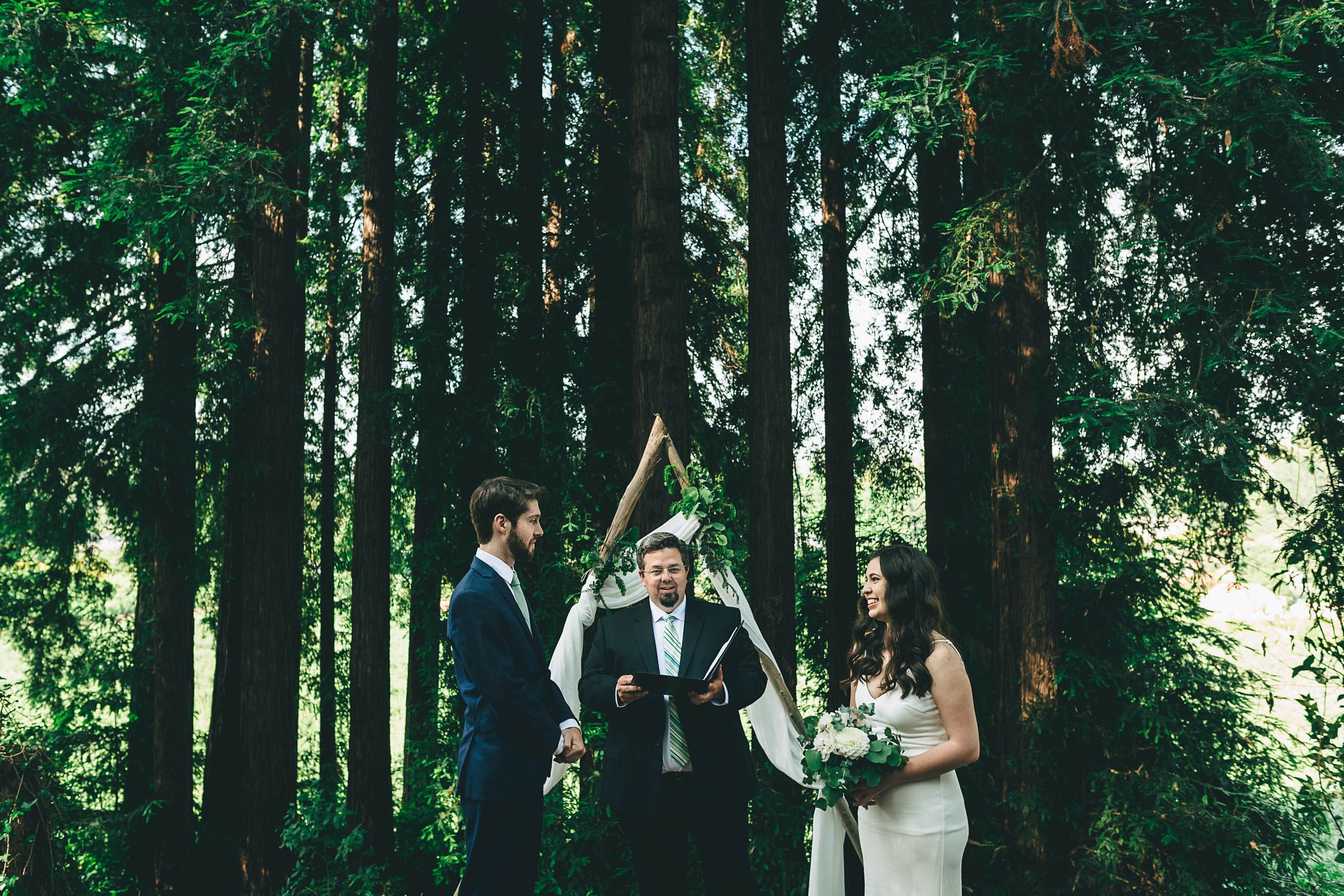 Bride and groom standing in front of wedding arch at their ceremony surrounded by redwoods