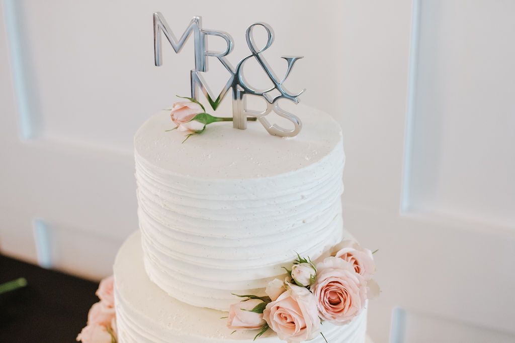 Elegant white tiered wedding cake with Mr & Mrs topper and pink rose accents.