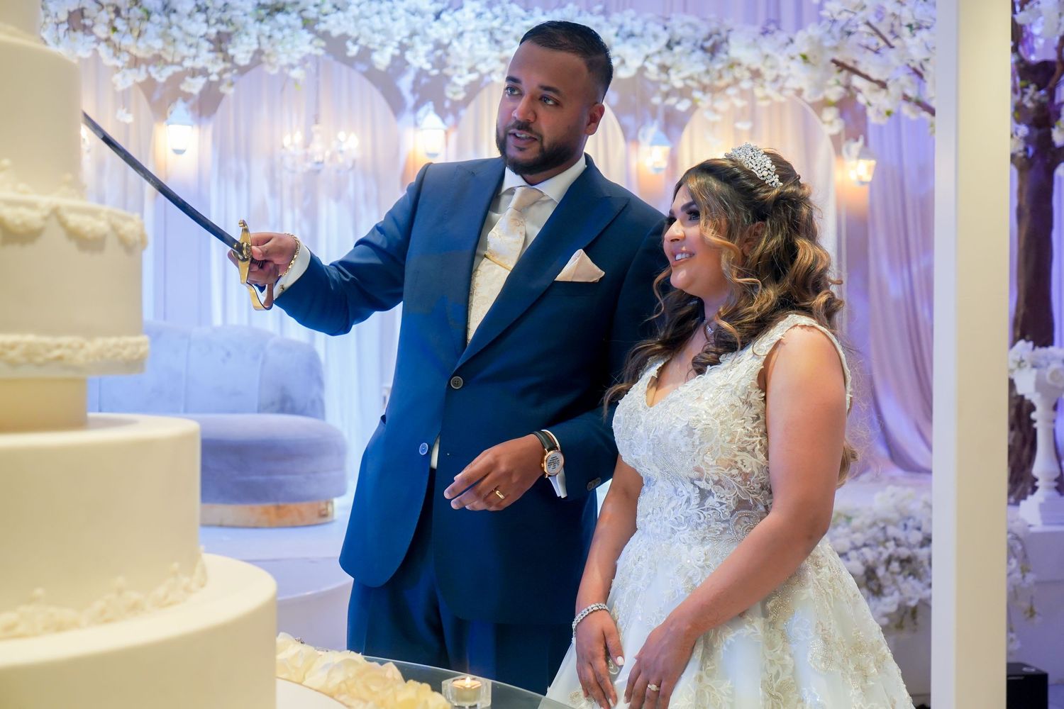 Wedding cake cutting ceremony with blue and white floral backdrop decoration.