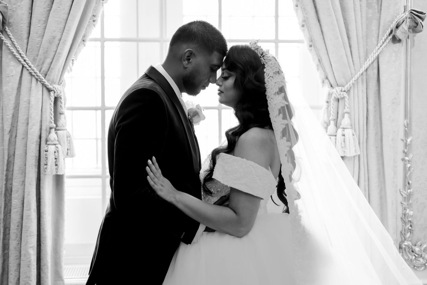 Black and white romantic wedding portrait with white lace curtains framing the couple.