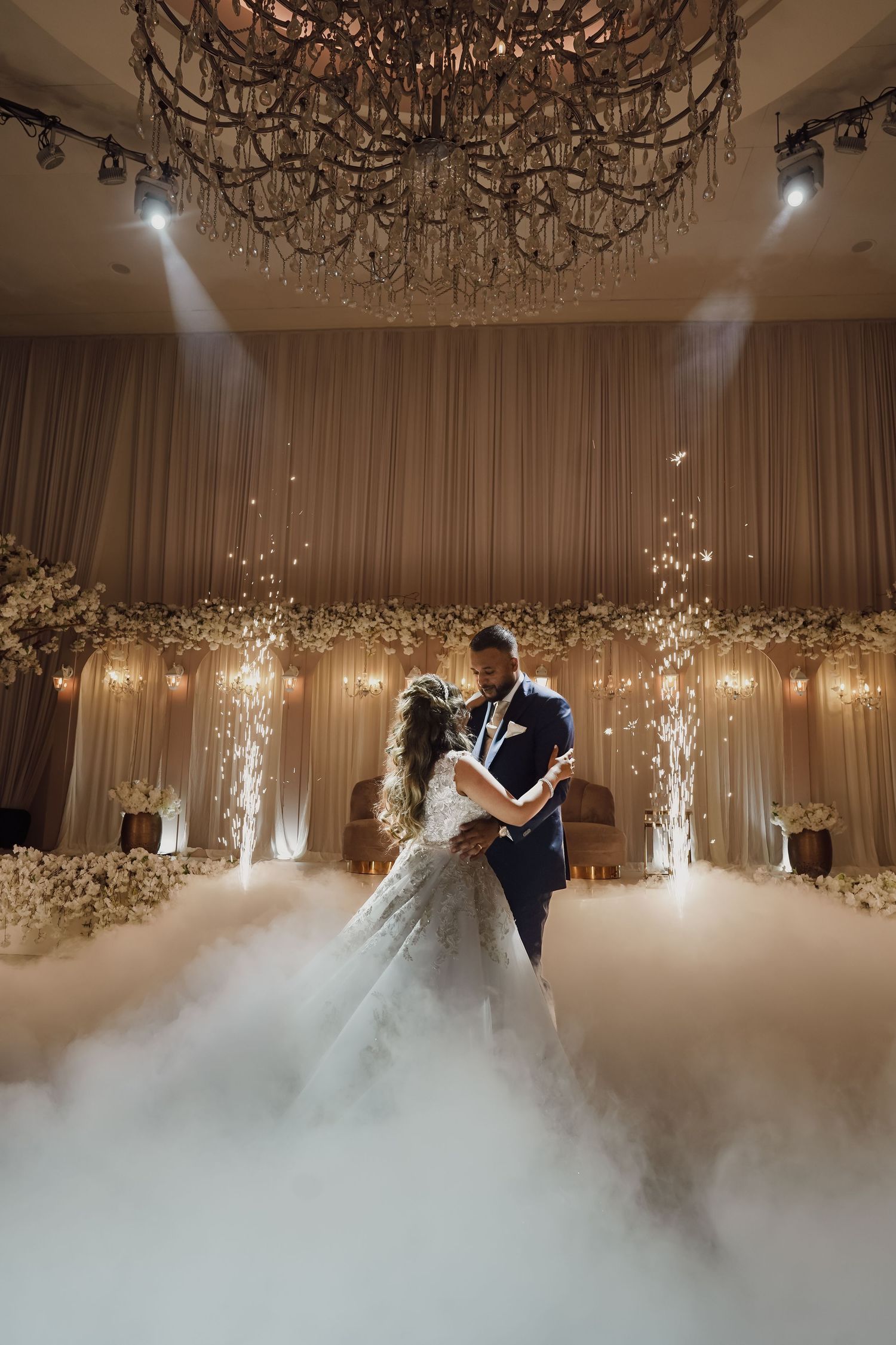 A romantic wedding ceremony with dramatic lighting, fog effects, and a grand chandelier in an elegant ballroom setting.