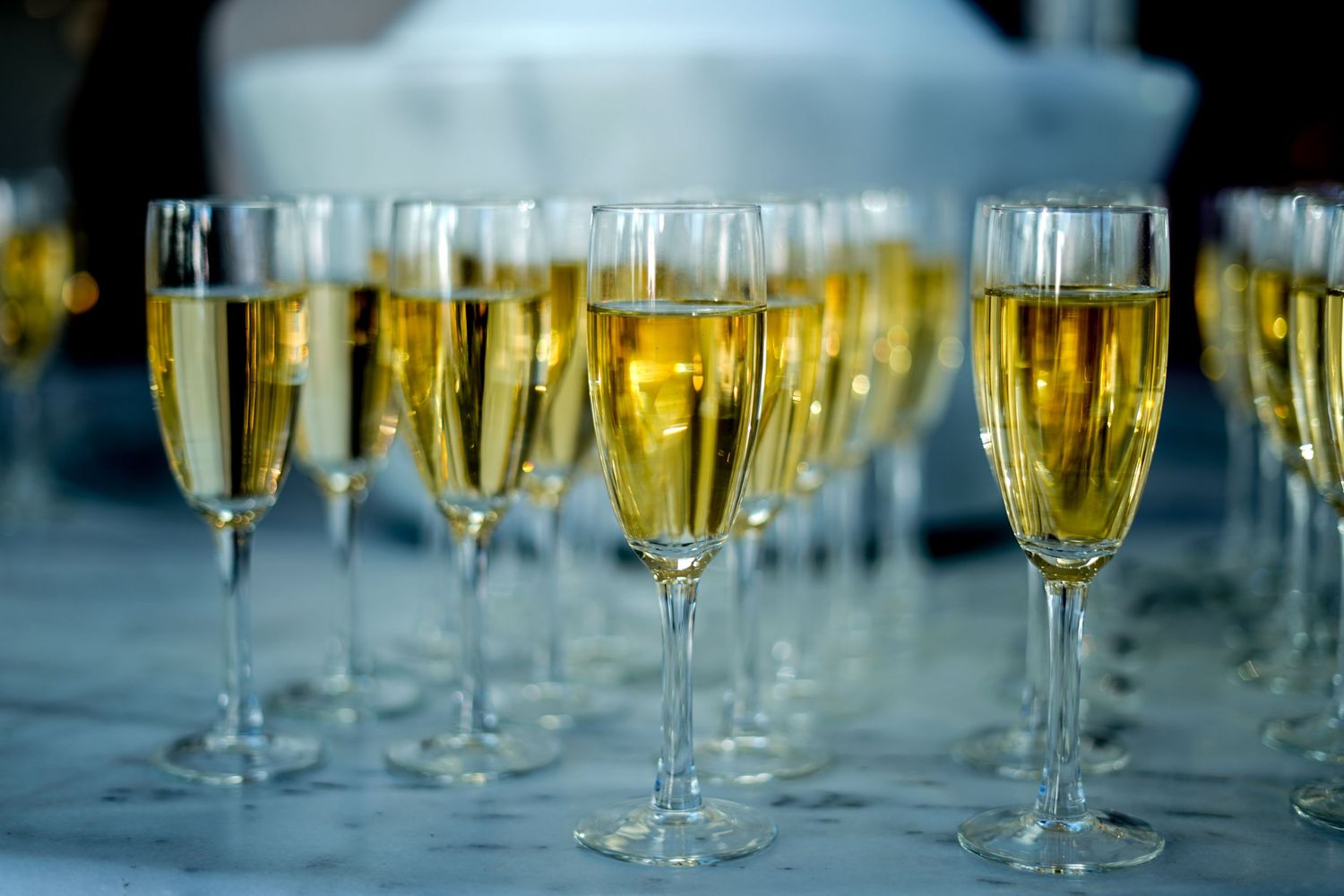 Multiple champagne flutes filled with sparkling wine on white tablecloth.