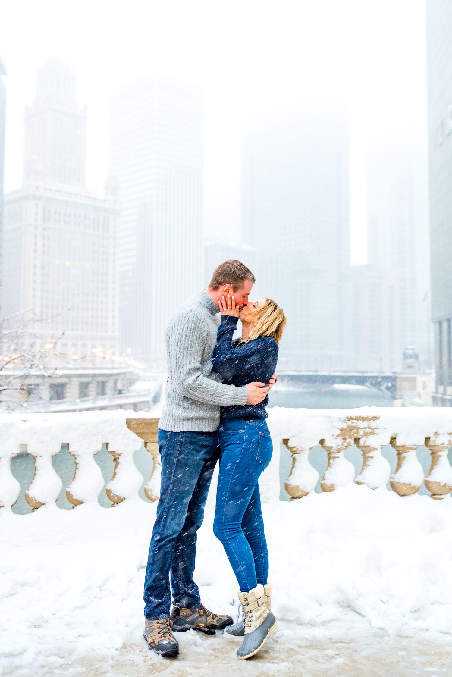 couple kissing in the snow at Wrigley Building overlooking the Chicago River for snowy winter engagement pictures