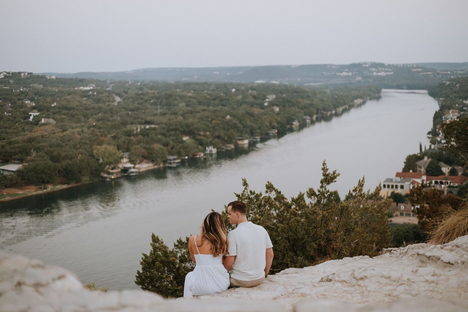 Newly engaged couple sitting together, gazing at the water in Austin, Texas, celebrating their engagement with a scenic view of nature.