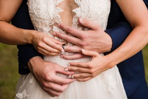 Close-up of hands with wedding rings embracing around a detailed lace wedding dress bodice.