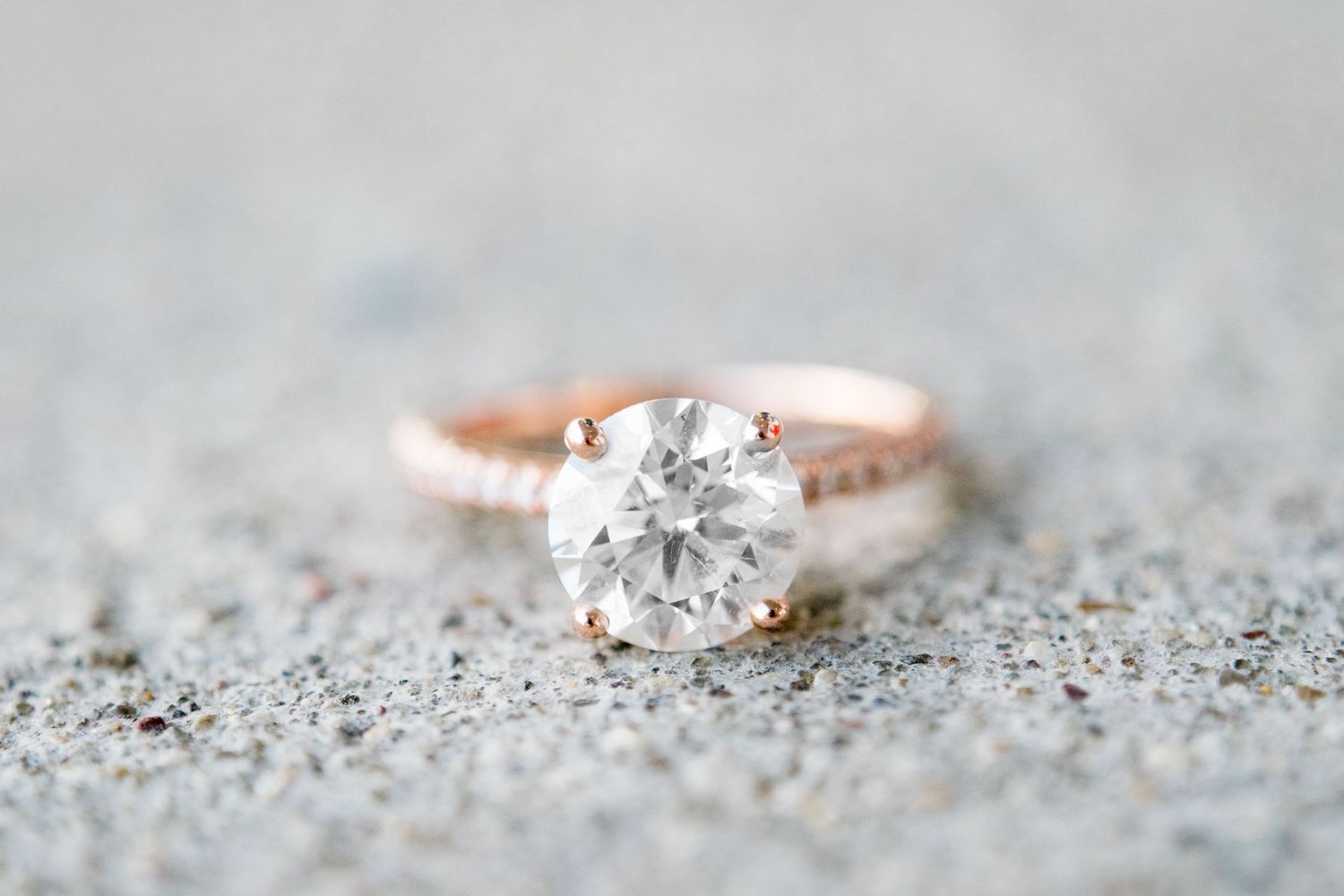close up of rose gold round diamond engagement ring on concrete