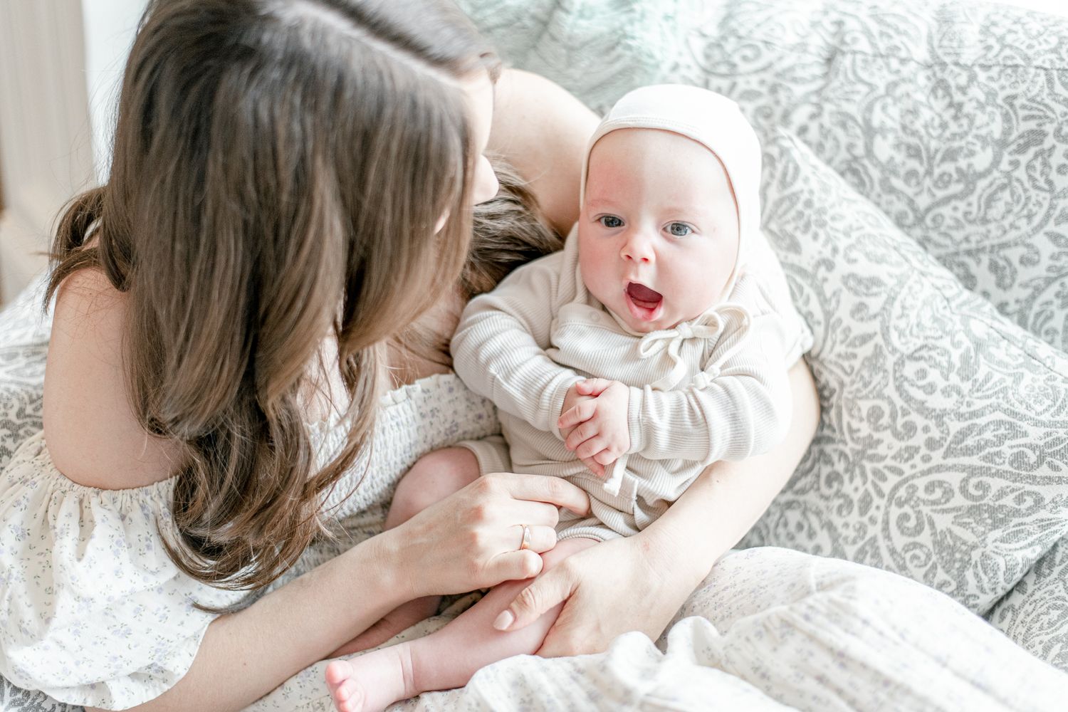 Baby boy with a bonnet yawns in his mothers arms