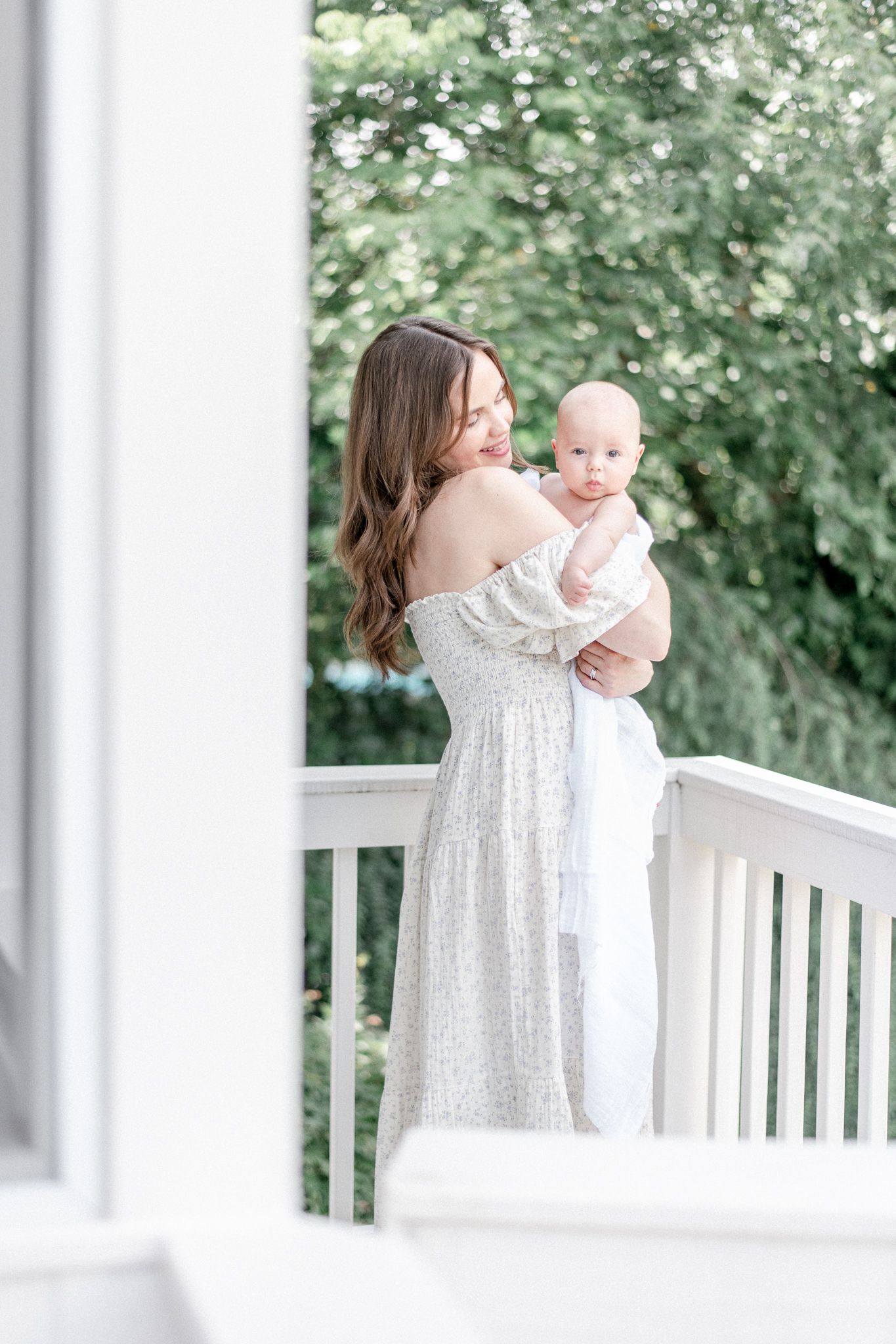 Mother stands on a white porch holding her baby boy