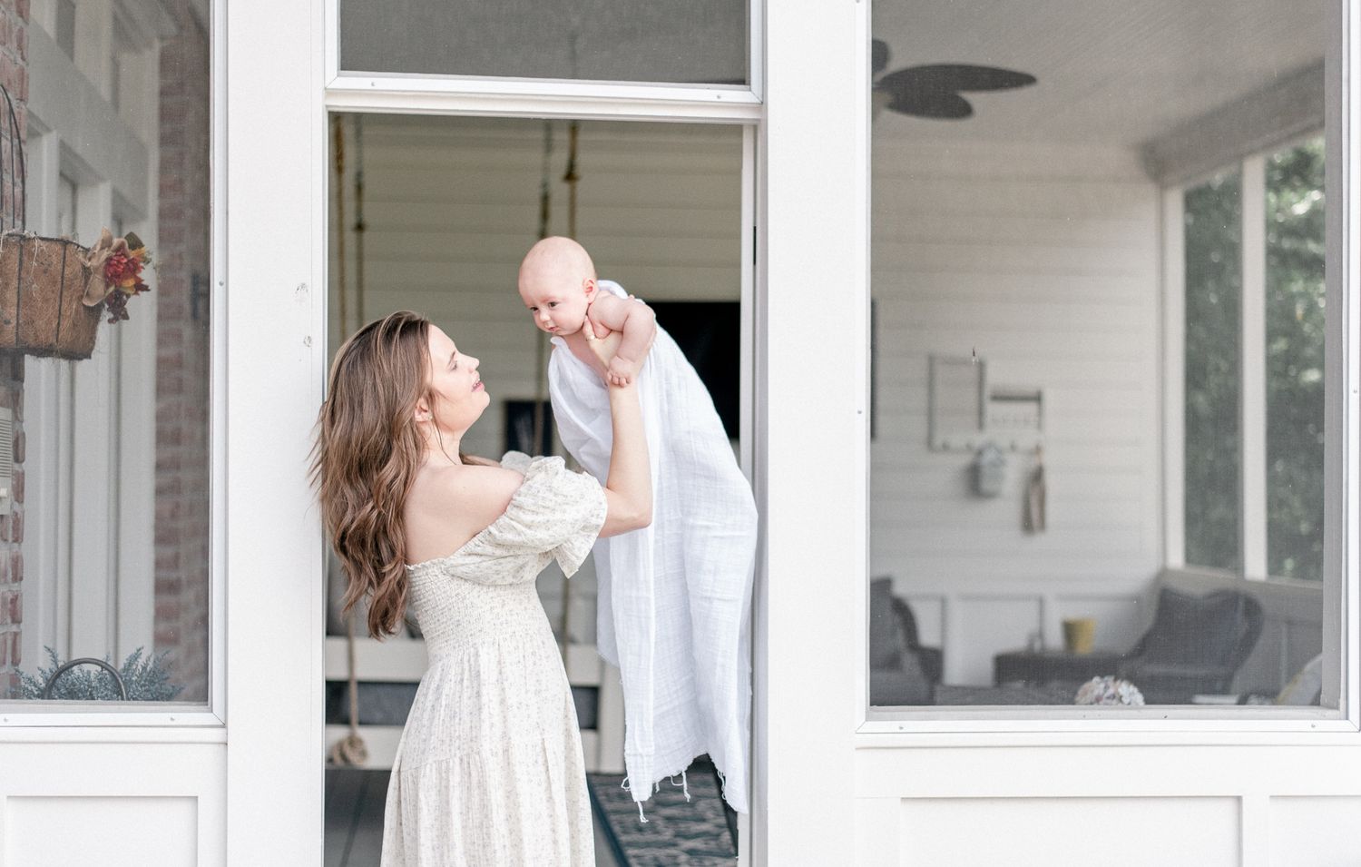 Mother holds her baby in the air on a white porch in Franklin, TN