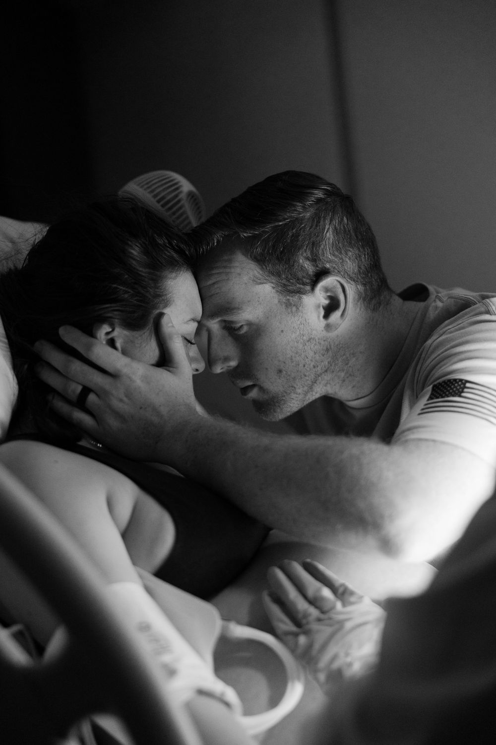 An intimate black and white photo of a tender moment between a couple lying close together.