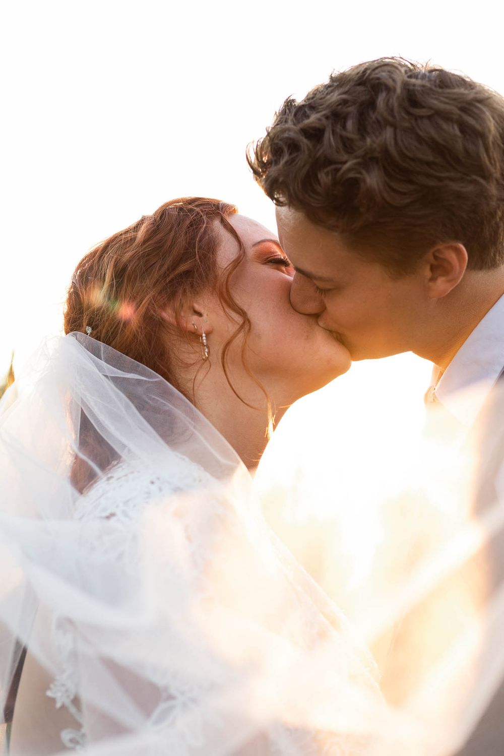 A close up of a bride and groom sharing a kiss while the sun shines through her veil at the Pondview Farm in Central, MN