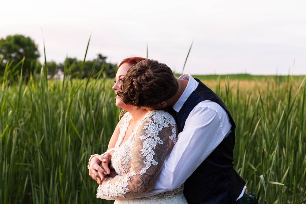 A groom wrapping his arms around his future bride while the sun sets on a reedy pond at Pondview Farms in Cambridge, MN