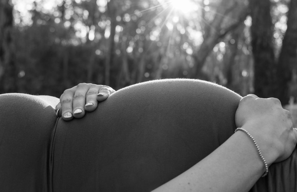 Black and white close-up of hands resting gently on a pregnant belly.