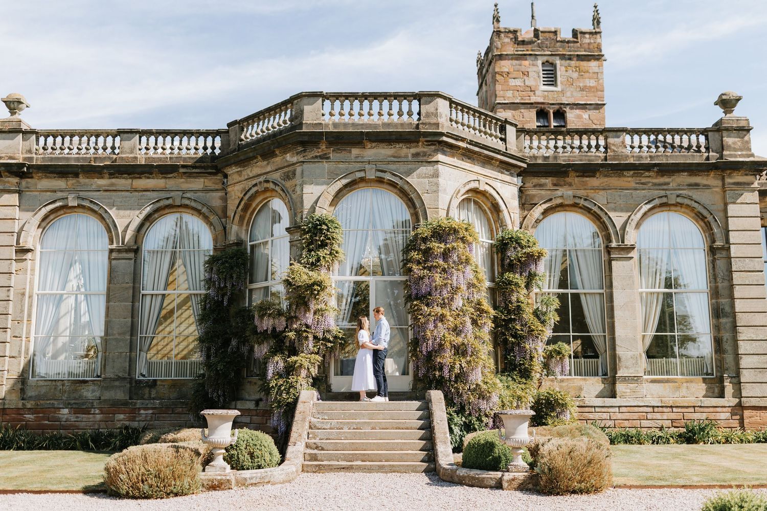 Elegant stone villa with grand archways, decorative balustrades, and lush garden terrace in the afternoon light.