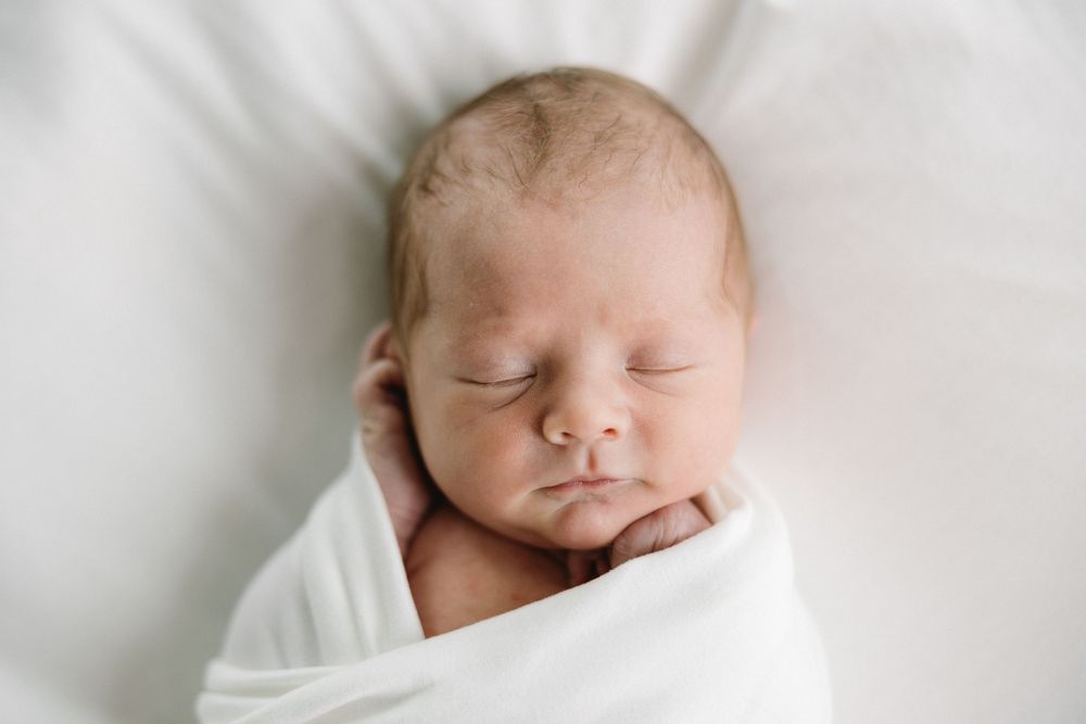 A sleeping newborn baby swaddled in soft white fabric against a white backdrop.