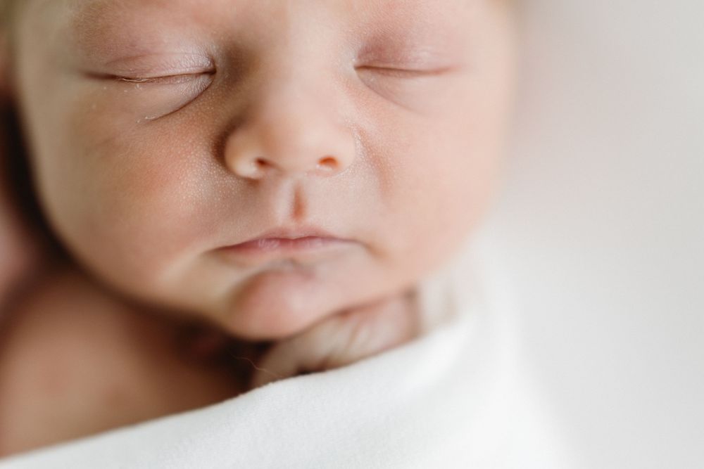 Close up macro shot of a sleeping newborn's peaceful face against white blanket.