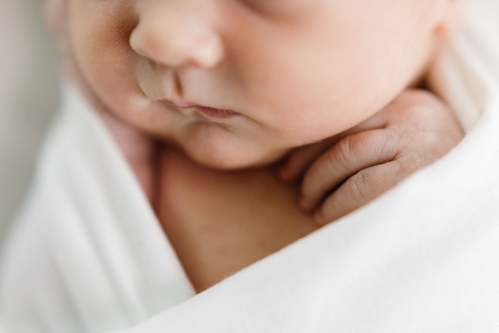 Peaceful close-up of a sleeping newborn swaddled in soft white fabric.