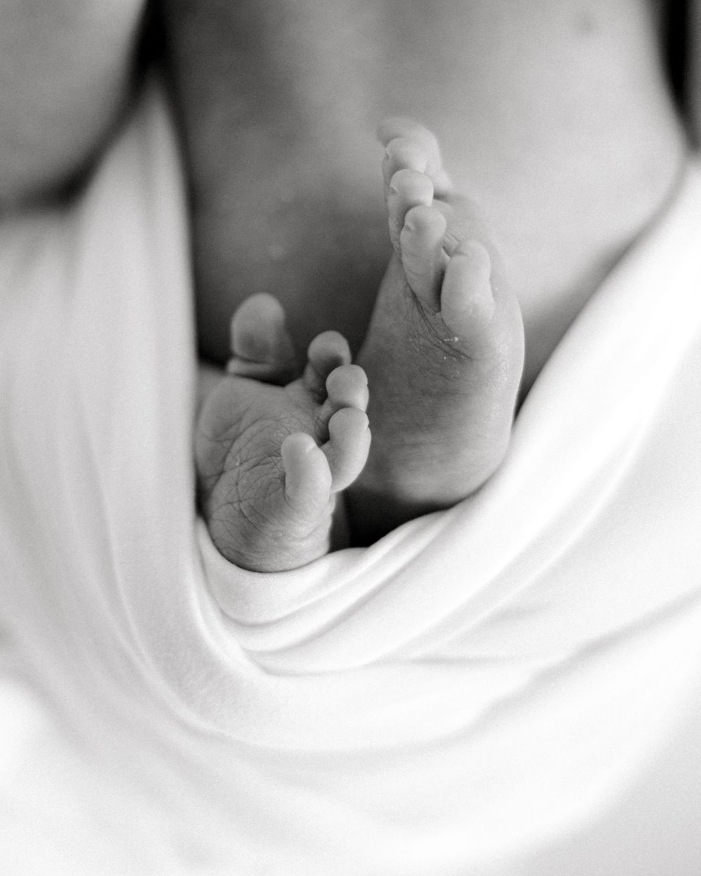 Black and white close-up of tiny newborn feet wrapped in white fabric.