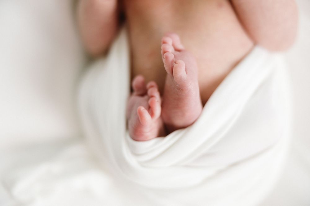 Soft focus image of small newborn feet peeking out from white fabric.