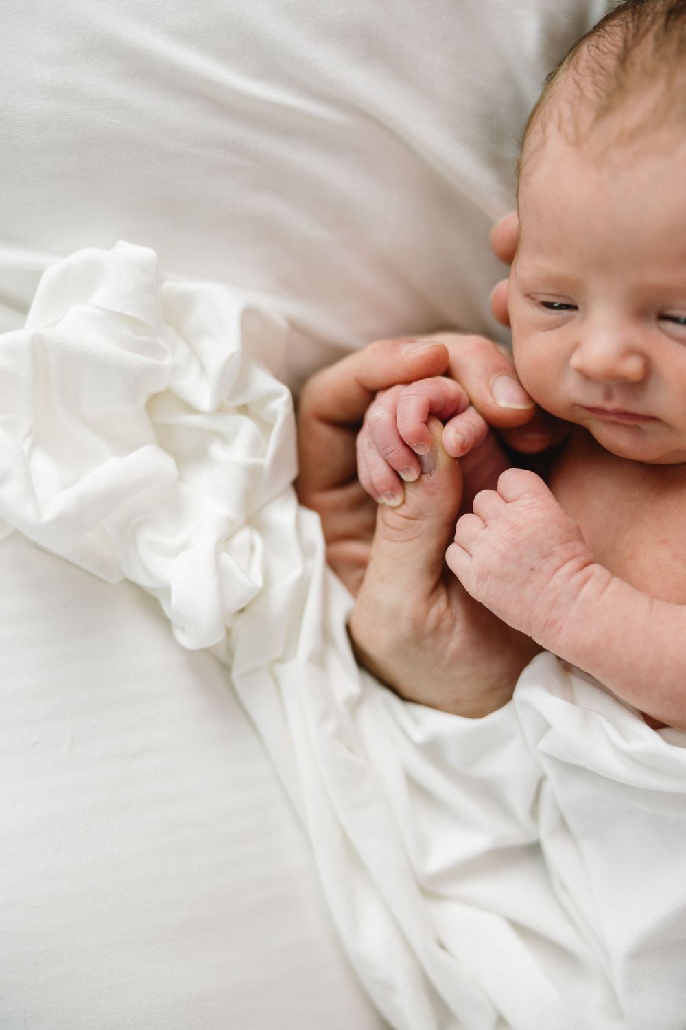 Peaceful newborn resting on white bedding with tiny curled fingers.