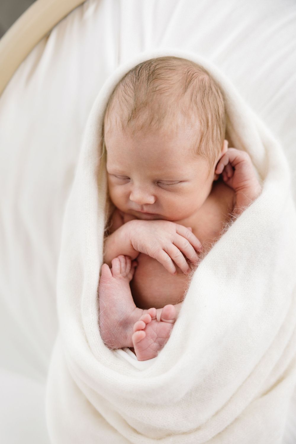 Sleeping newborn wrapped in soft white fabric in artistic portrait style.
