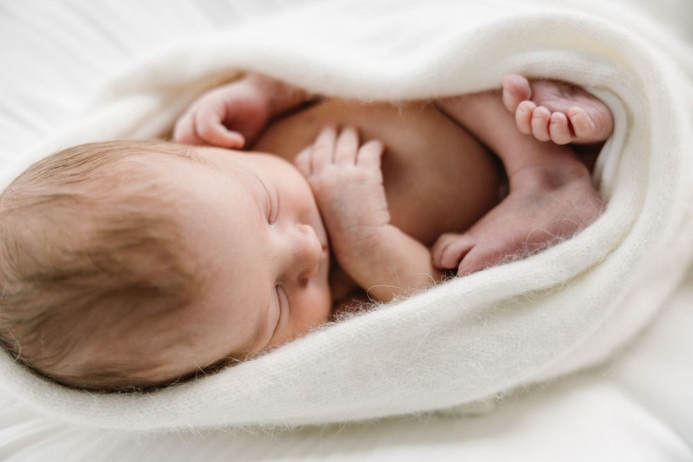 Side view of sleeping newborn cradled in white blanket.