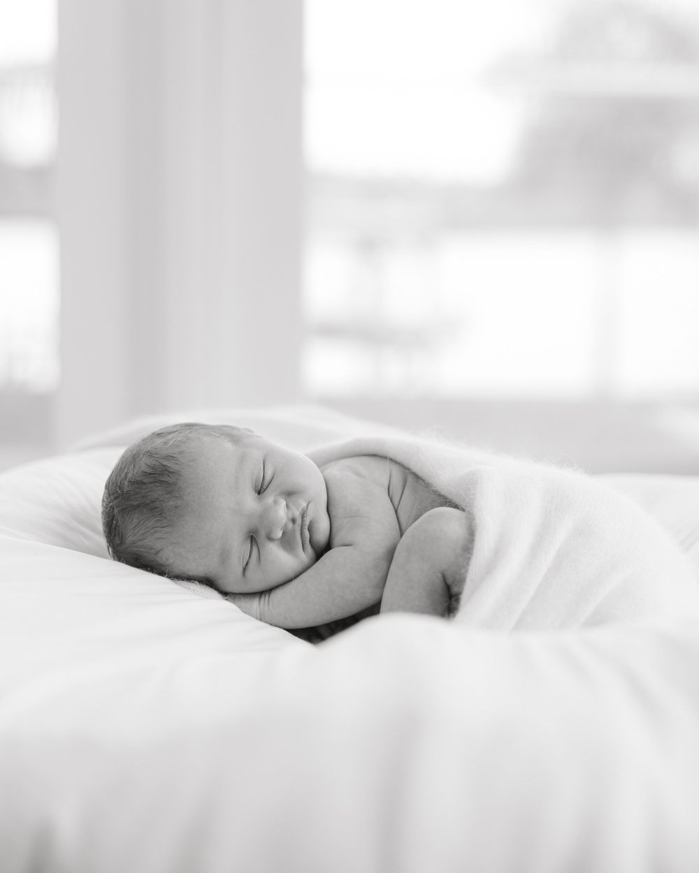 Black and white portrait of sleeping newborn wrapped in soft blanket.