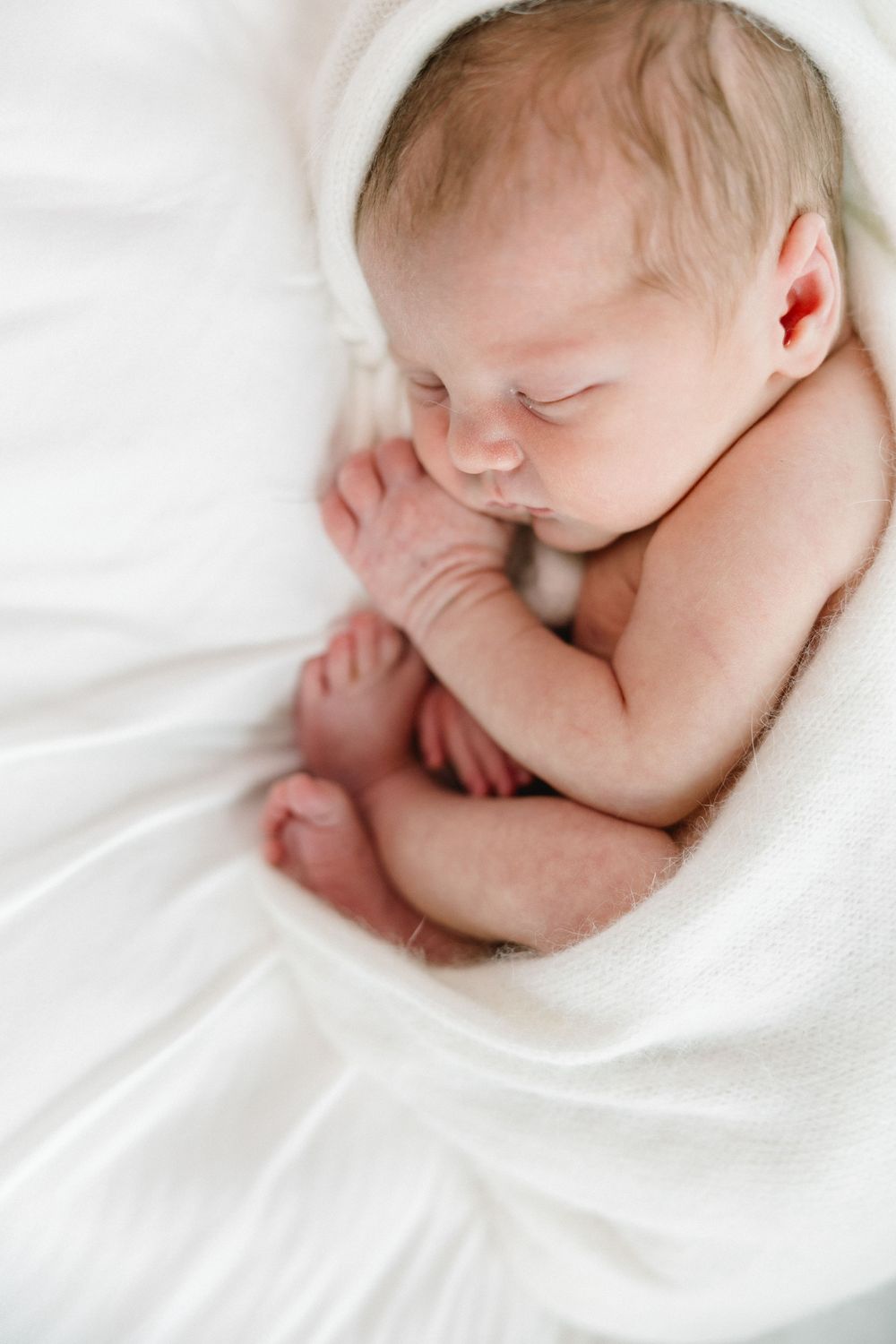 Overhead view of sleeping newborn nestled in white fabric.