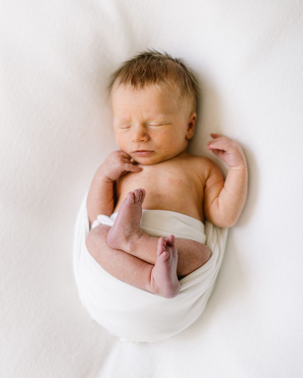 Peaceful sleeping newborn baby swaddled in white fabric on light backdrop.