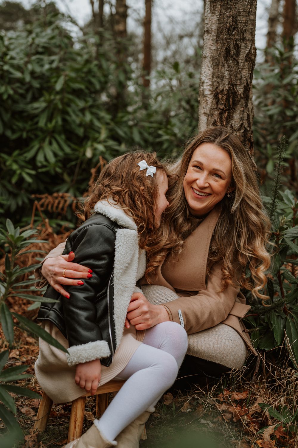 Candid and joyful interaction between parent and child sitting together against a tree in a natural forest setting.