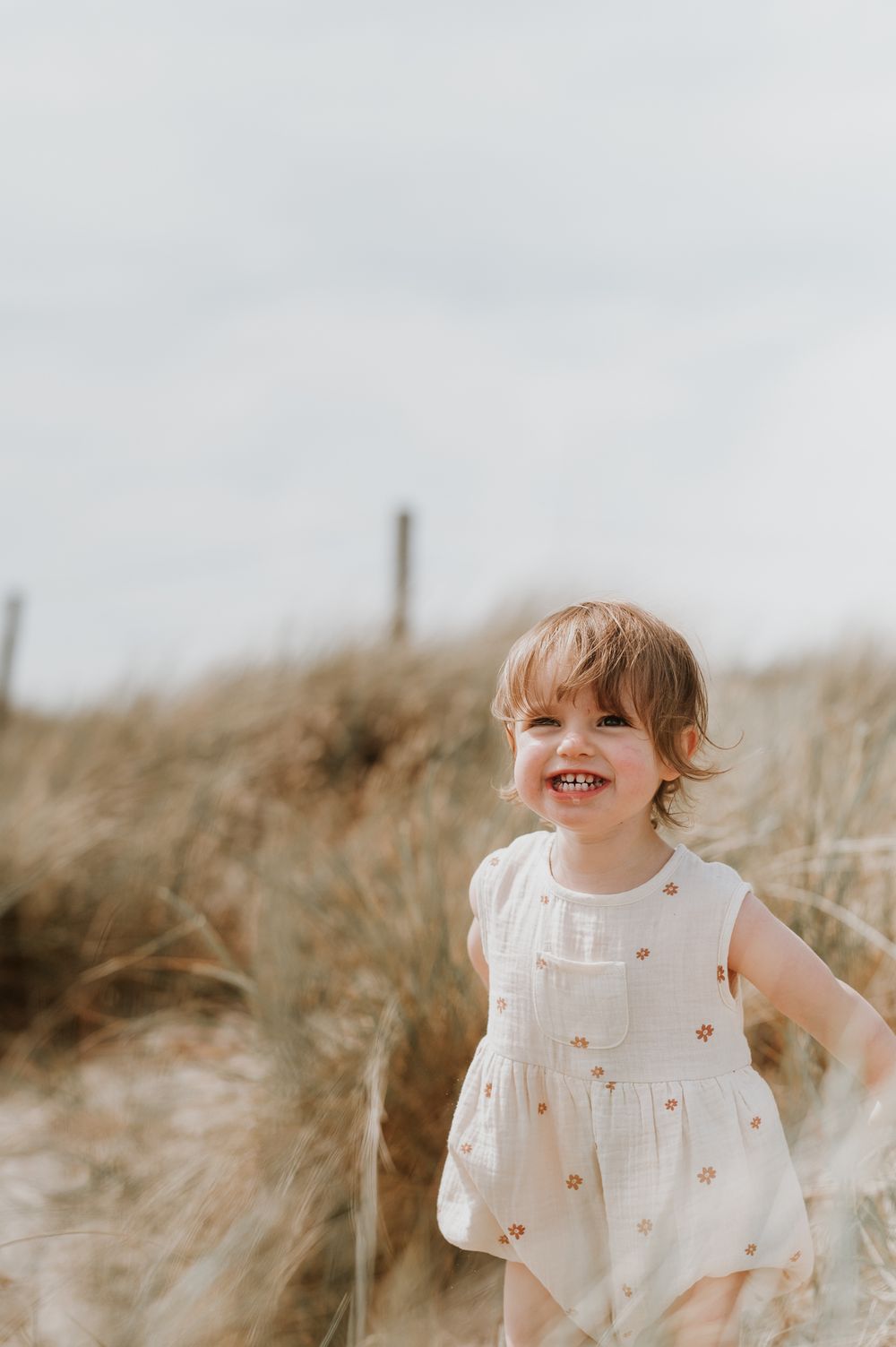 A child wearing a white dress plays in tall golden grass during sunset on a warm summer evening.