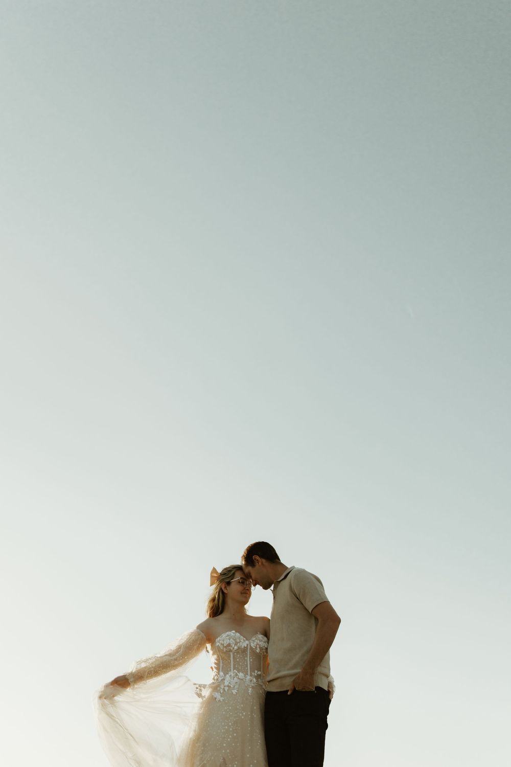 A romantic couple in wedding attire lean close together against a minimalist light background.