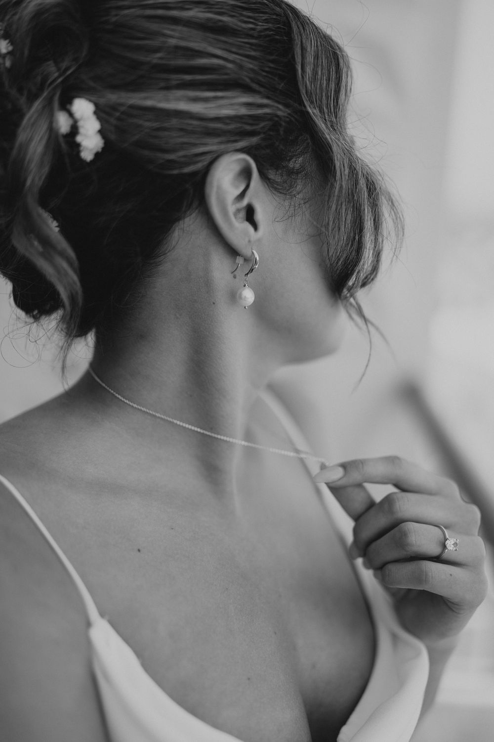 Elegant black and white close-up photograph showing pearl earring and delicate white dress strap on graceful neck.